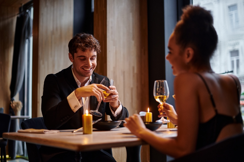 happy man in evening attire holding glass of wine and having dinner with woman in restaurant while having a meaningful conversation